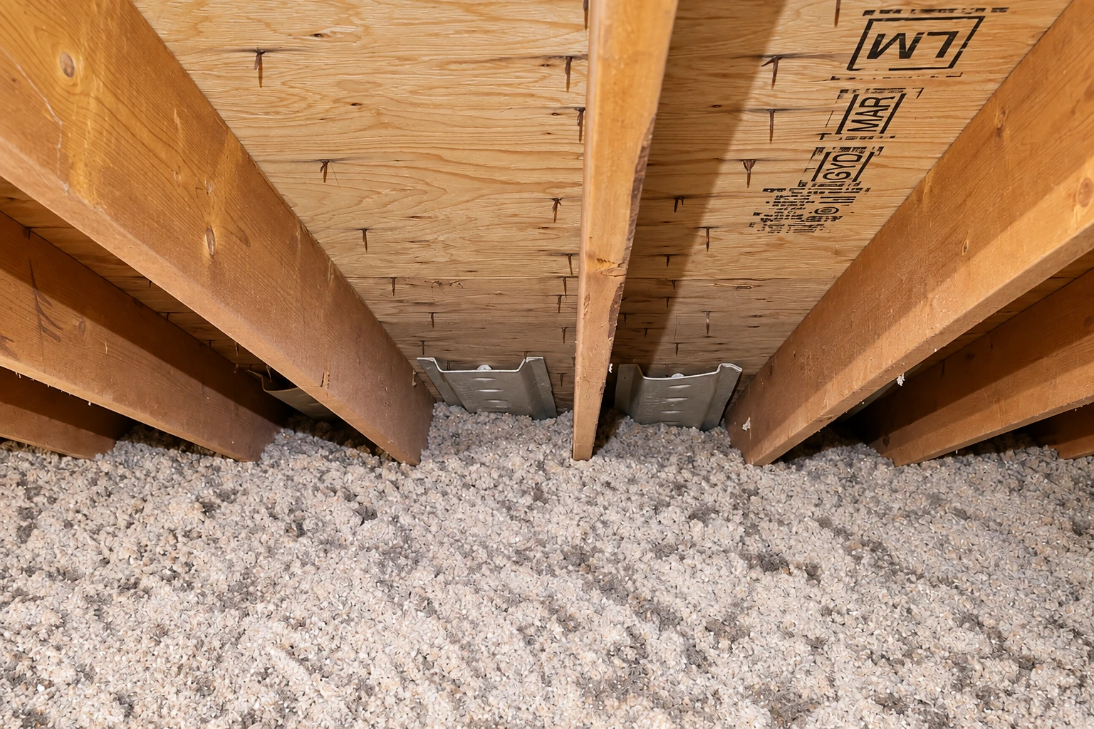 Loose-fill insulation spread across an attic floor beneath exposed wooden rafters.