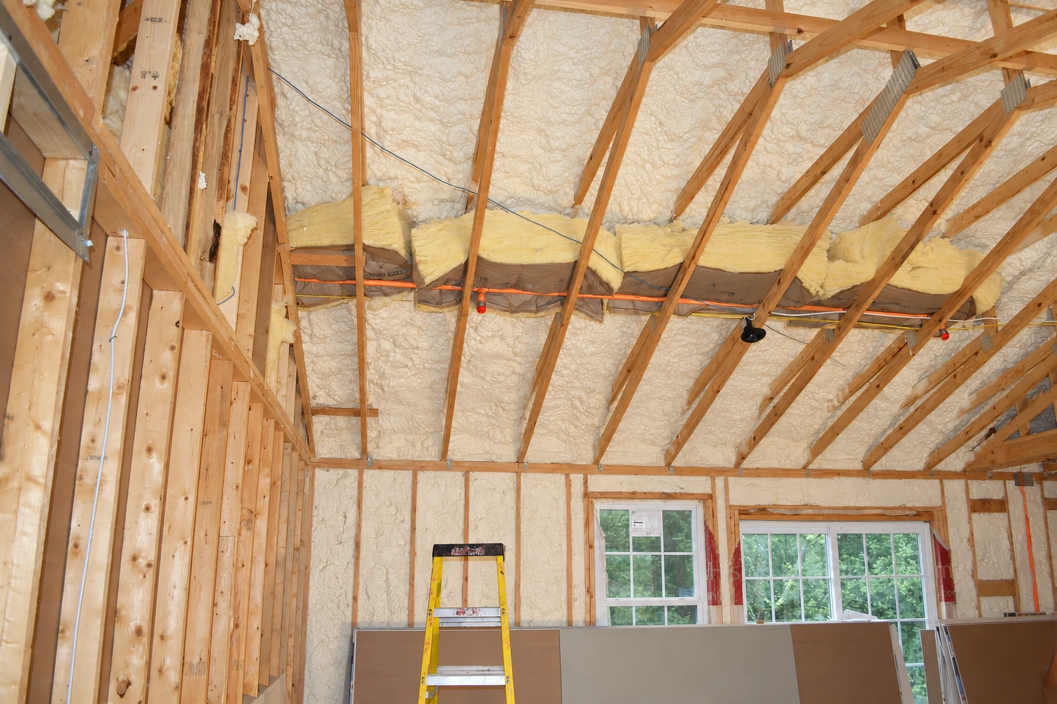 Unfinished room with white spray foam insulation covering the roof and walls between exposed wooden framing.